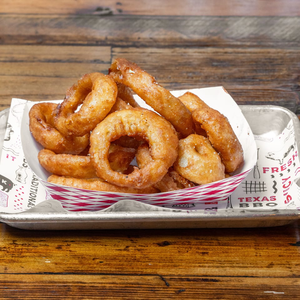 Basket of golden-brown fried onion rings served on branded paper in a metal tray atop a rustic wooden table.