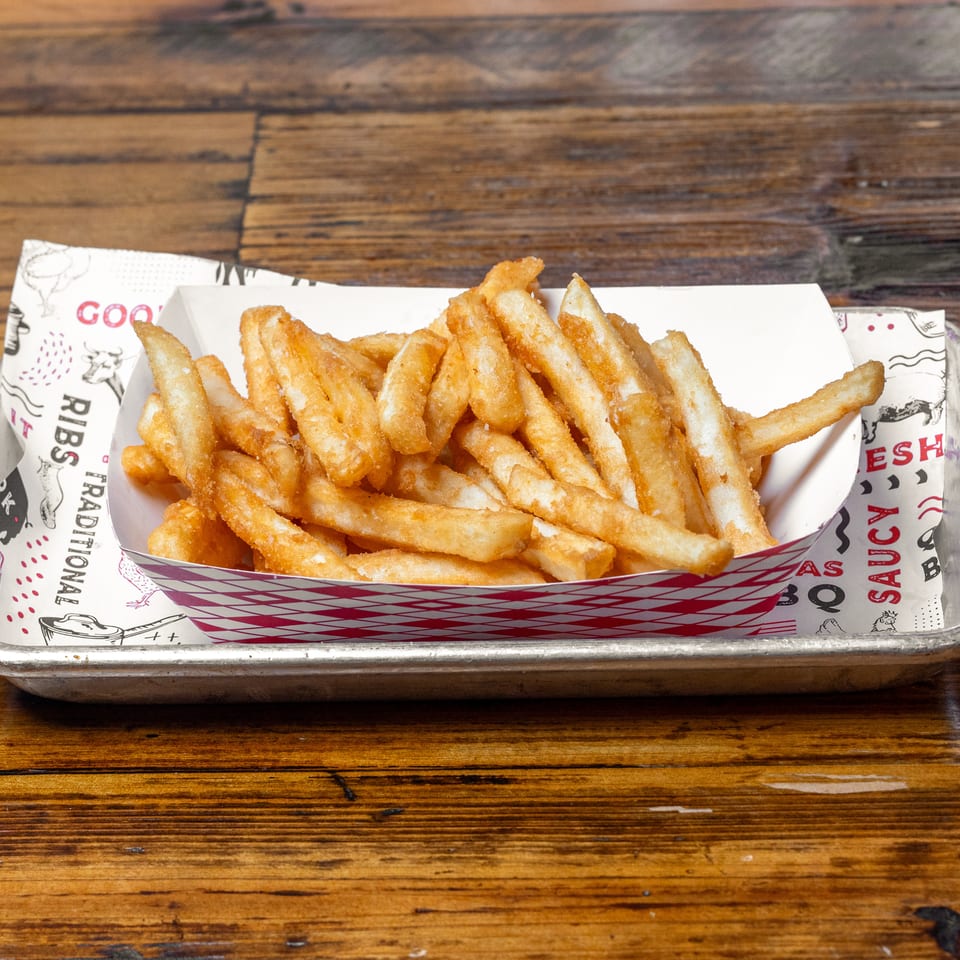 Crispy golden fries piled in a red-and-white checkered paper tray on a metal serving platter atop a wooden table.