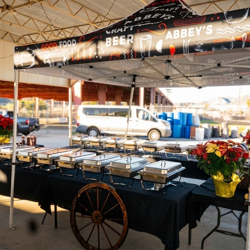 Abbey’s beer food booth with covered buffet tables, holiday poinsettias, picnic seating, and an industrial outdoor setting.